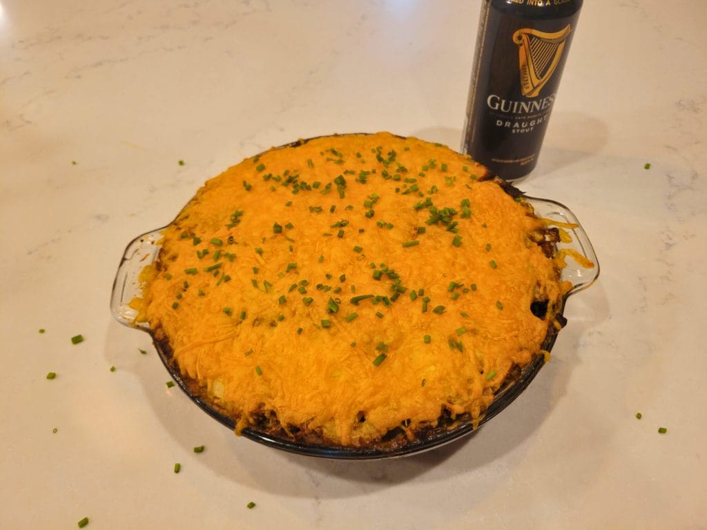 guinness shepherd's pie in a glass pie dish, garnished with chopped chives next to a black can of guinness stout